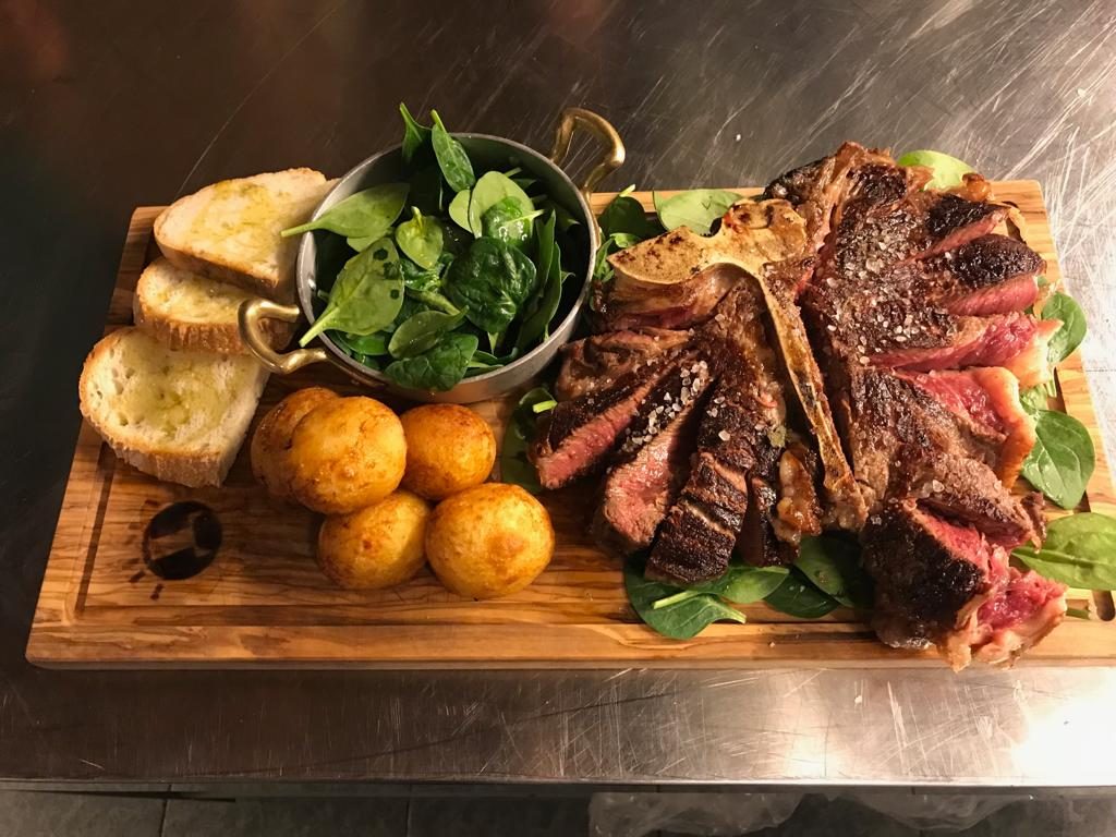Florentine Steak with Roast potatoes, Tuscan bread and fresh salad on a rustic wooden board